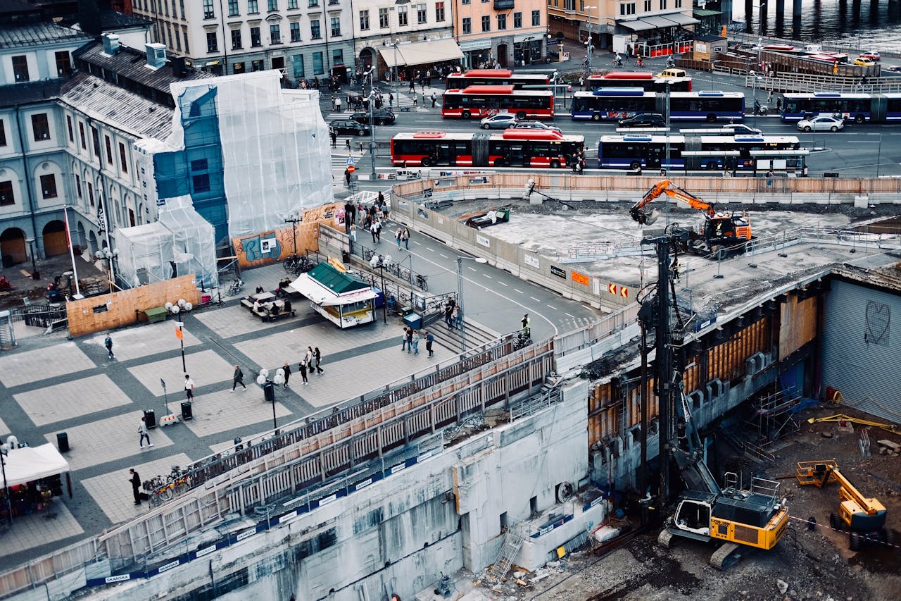 Aerial view of urban construction site in Norrmalm with buses and pedestrians, showcasing city life.